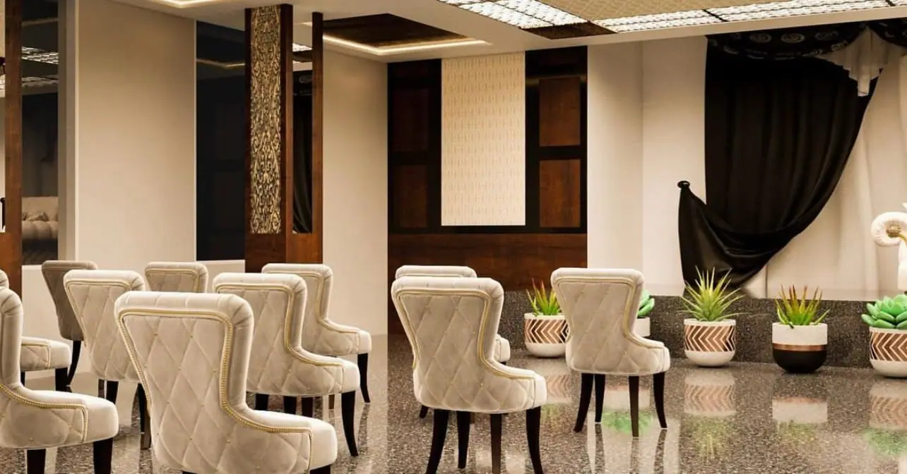 Banquet hall seating beside the stage, with gold-bordered tufted chairs, carved column panels, black drapes and planters on the stage edge