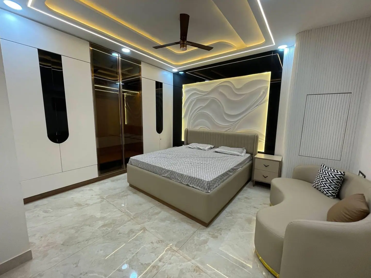 Master bedroom with a sculpted wave-pattern headboard wall, cove-lit false ceiling and full-height wardrobes